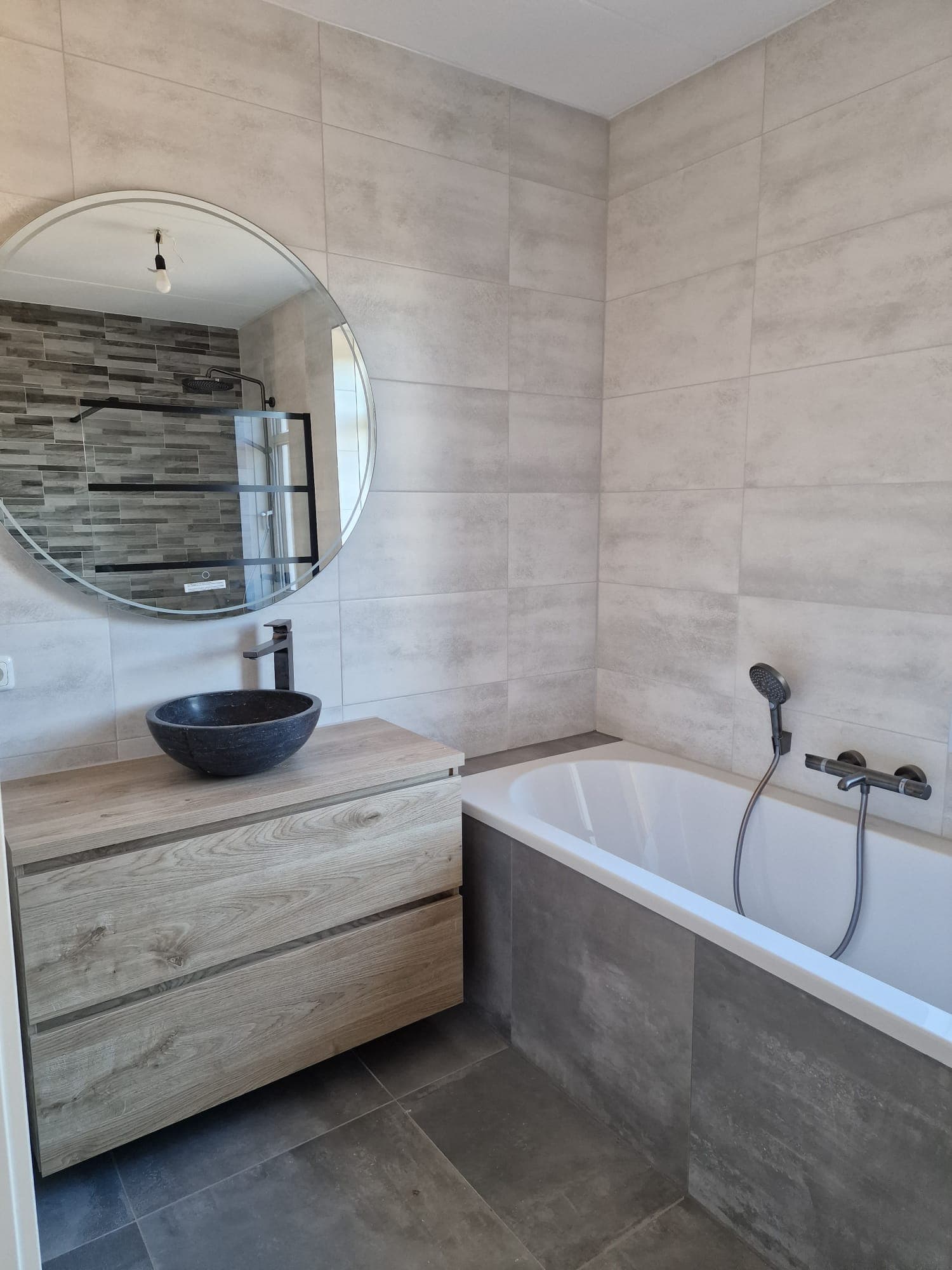 Gerenoveerde badkamer met ligbad, badmeubel met eikenhoutlook, waskom, ronde spiegel en lichte wandtegels