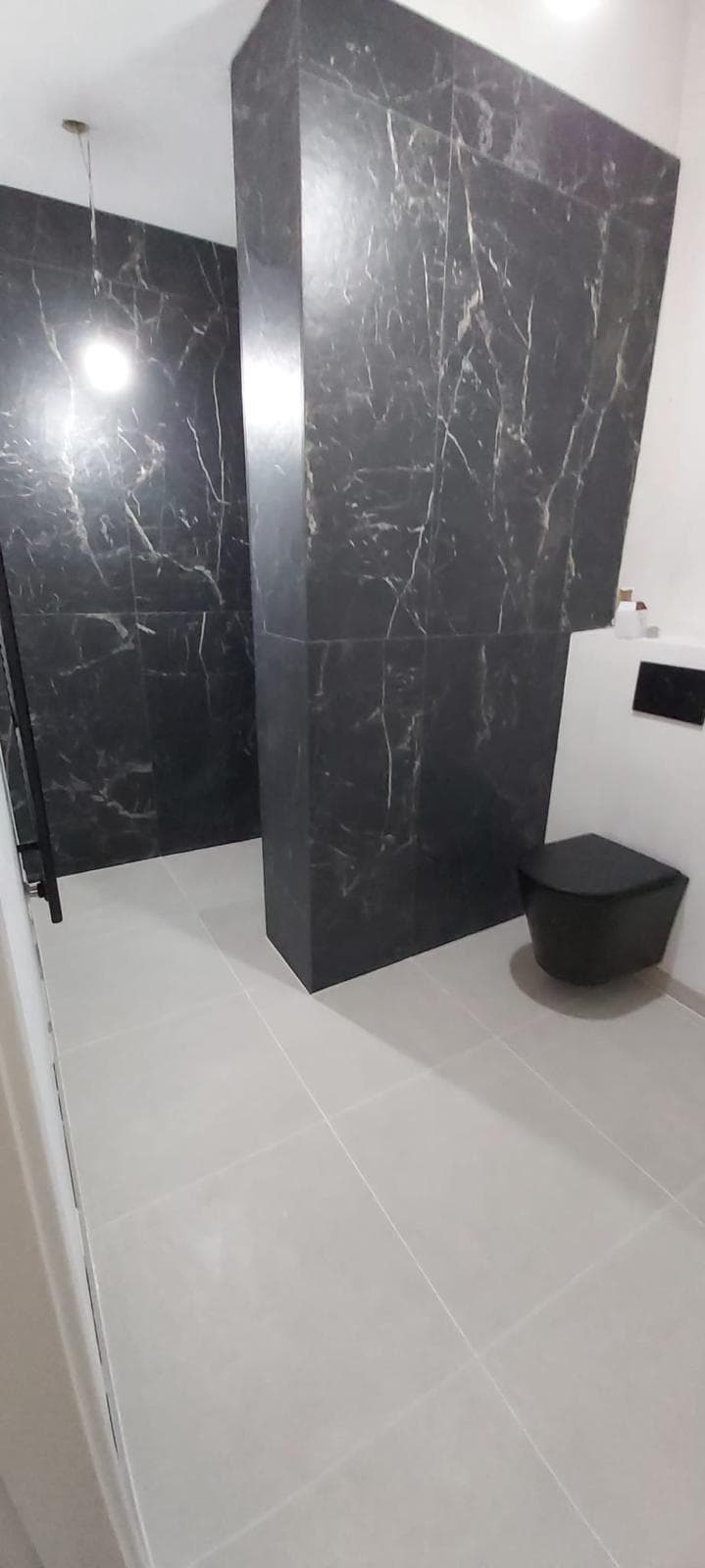 Badkamer met zwarte tegels in marmerlook in de douche, lichte vloertegels en een zwart hangtoilet
